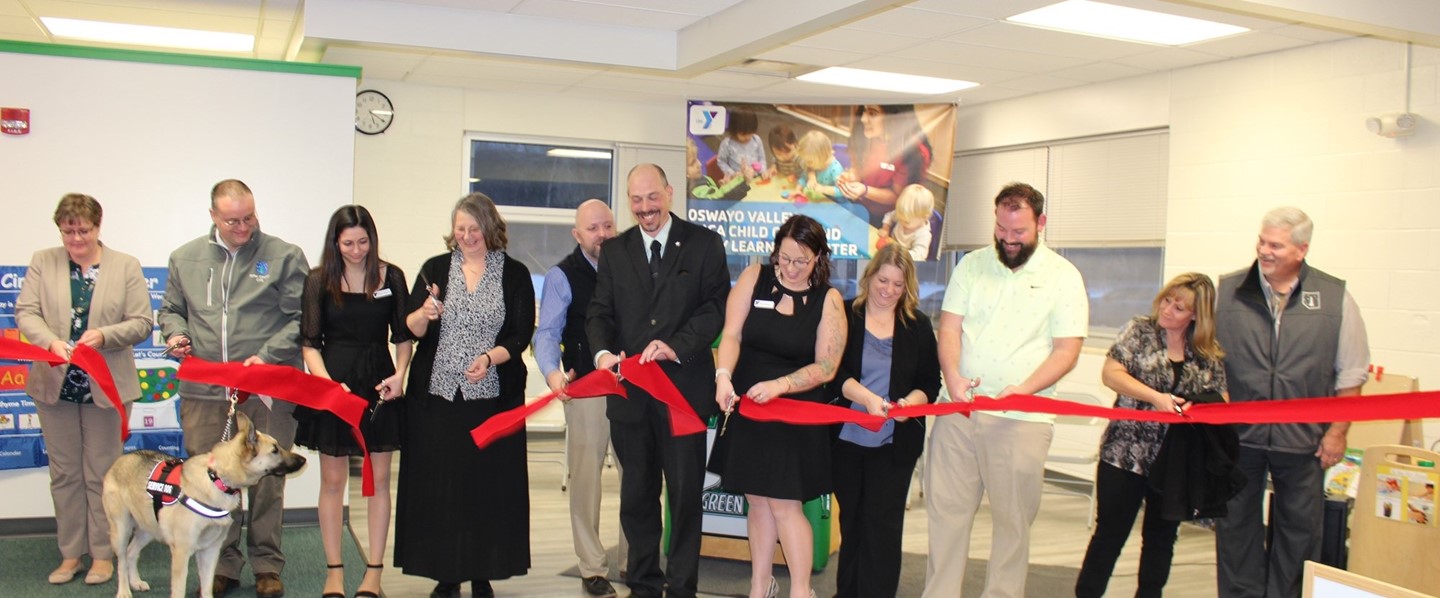 Group of people cutting red ribbon at grand opening 