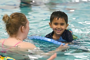 Young boy in swimming pool with adult instructor